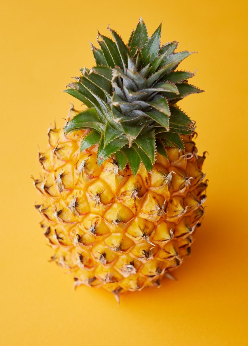 From above of fresh whole exotic pineapple with textured shell and green crown placed on yellow table